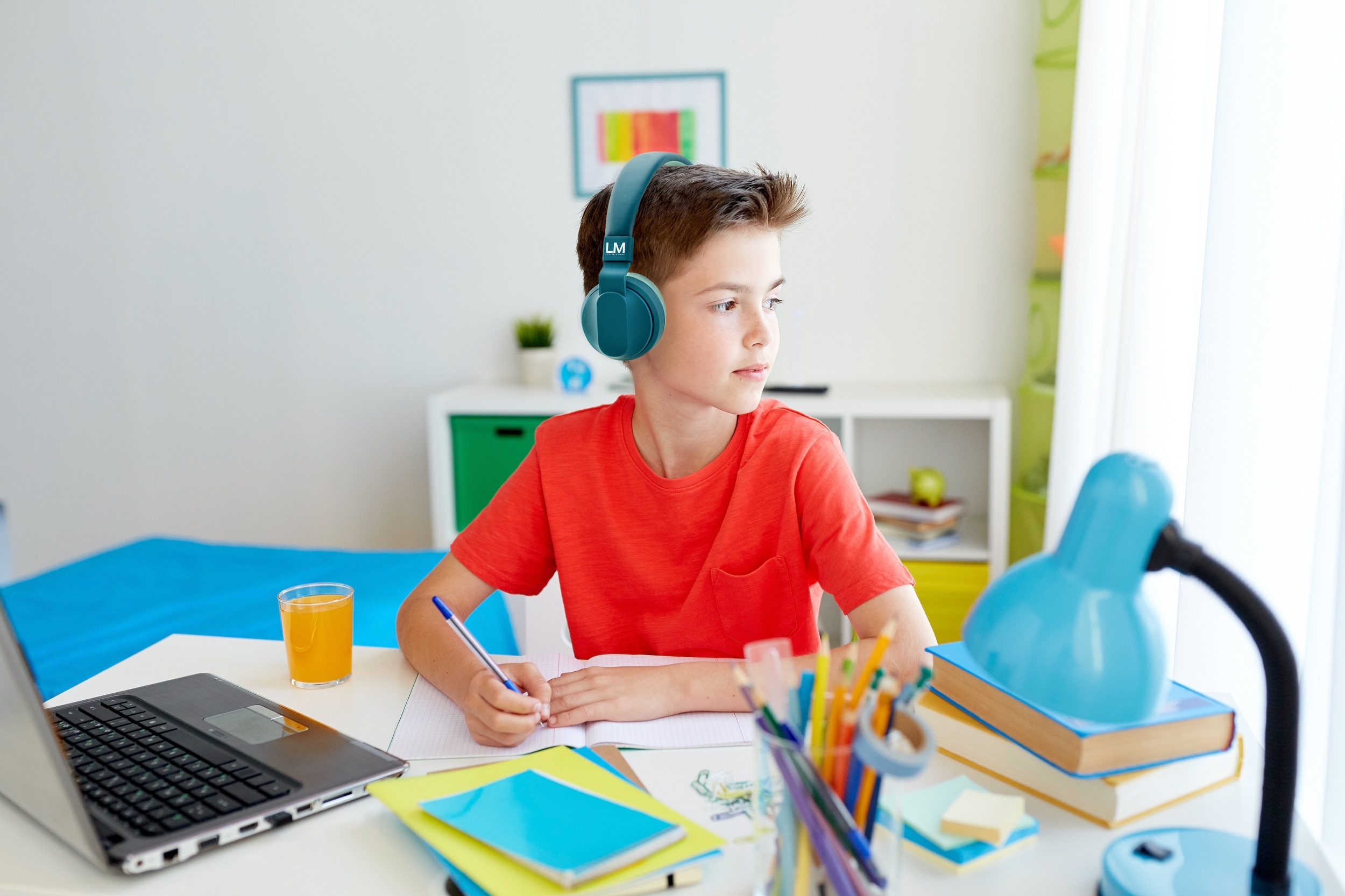 education, childhood and people concept - happy student boy with laptop computer writing to notebook at home